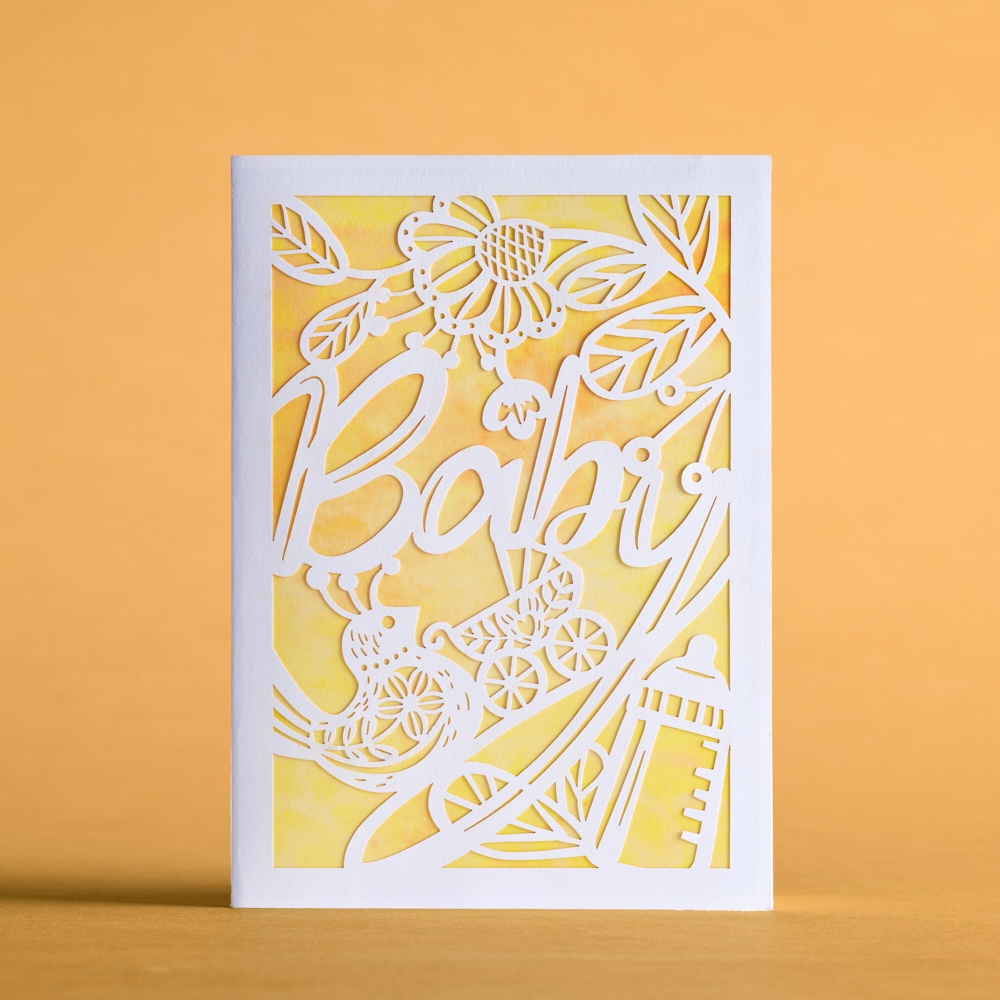 Yellow and white Baby Carriage Moments greeting card standing on a wooden surface