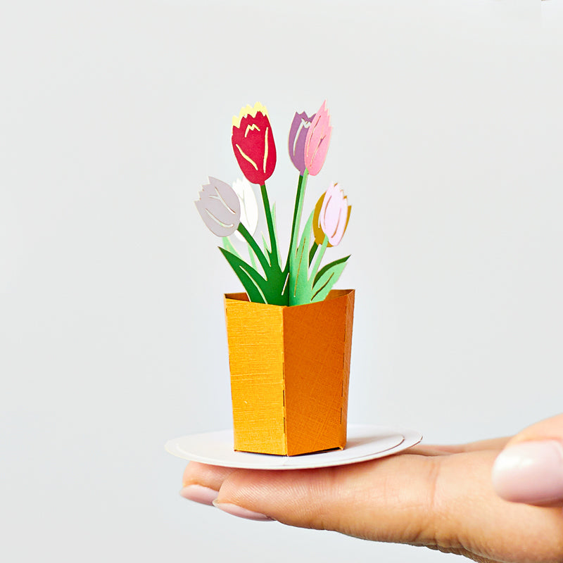 Small red, pink and white paper tulips in a yellow container on a fingertip